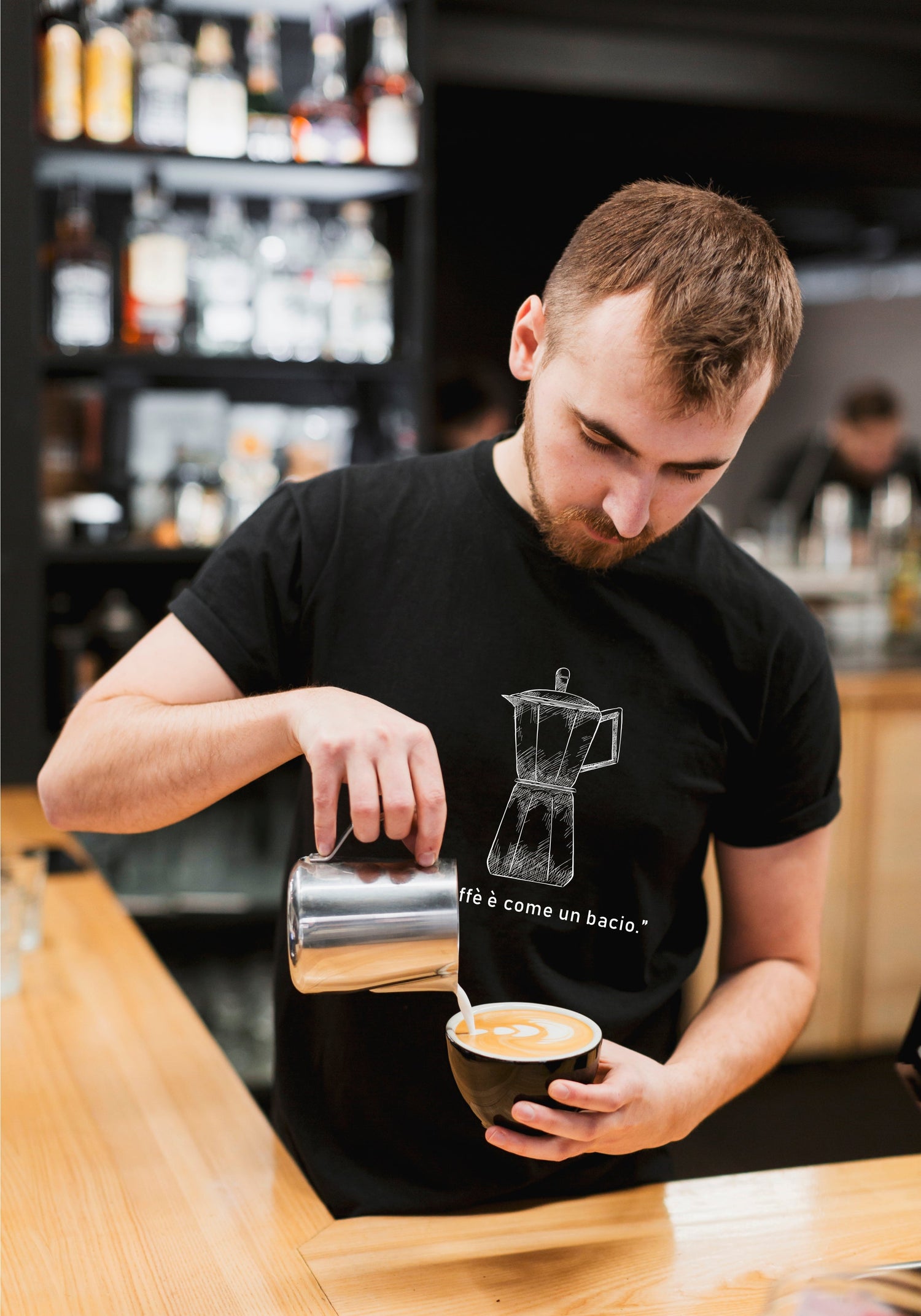 „Model trägt das schwarze Bio-Baumwoll-T-Shirt mit italienischem Spruch ‚Il Caffè è Come un Bacio‘, lässiger urbaner Look.“