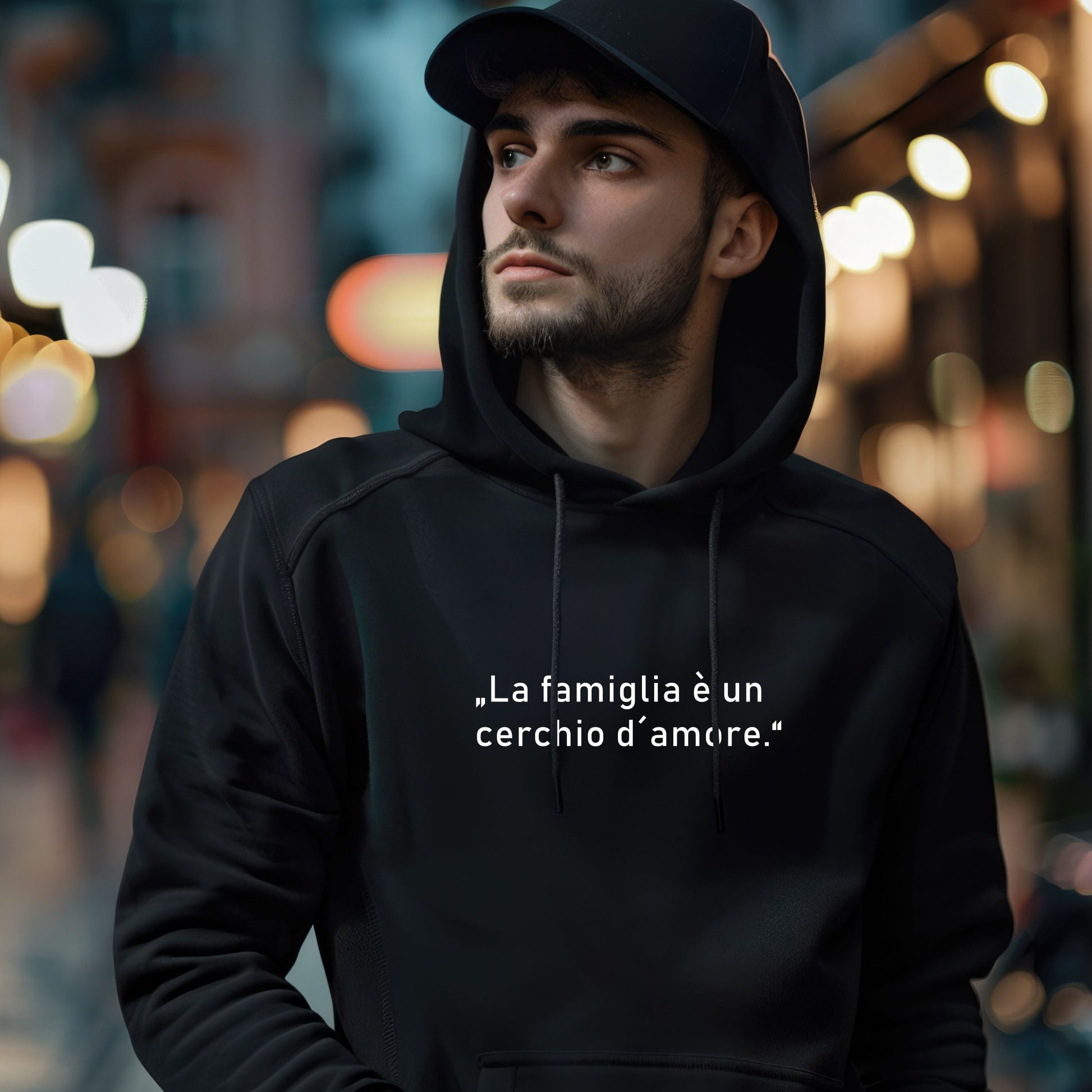 Person mit schwarzer Cap trägt schwarzen Hoodie mit weißem italienischen Zitat „La famiglia è un cerchio d’amore“, fotografiert bei Nacht auf einer beleuchteten Stadtstraße