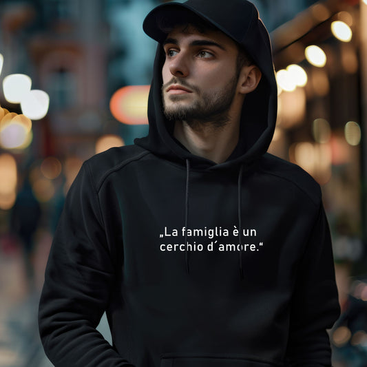 Person mit schwarzer Cap trägt schwarzen Hoodie mit weißem italienischen Zitat „La famiglia è un cerchio d’amore“, fotografiert bei Nacht auf einer beleuchteten Stadtstraße