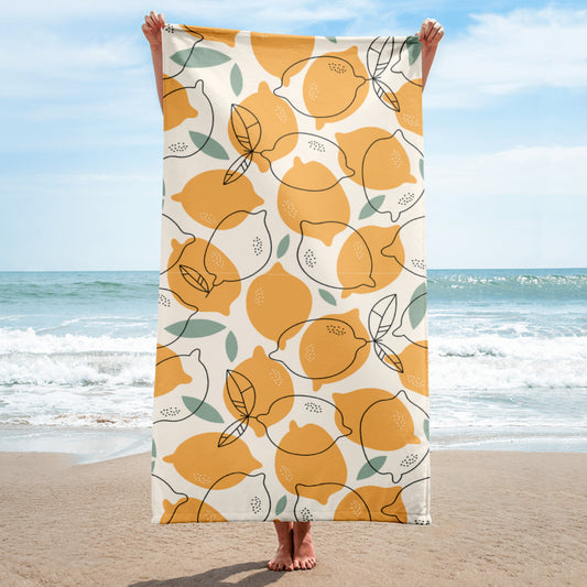 Person hält ein großes Handtuch mit gelbem Zitronenprint und grünen Blättern am Strand

